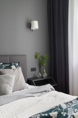 Büyük yataklı, sade ve rahat bir yatak odası süslemeleri ve koyu perdeleri olan şık bir komodin.