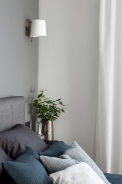 Yatak odasının köşesine yakın çekim. Yatağın yanındaki lambanın altında bir sürü yastıkla süslemeler var.