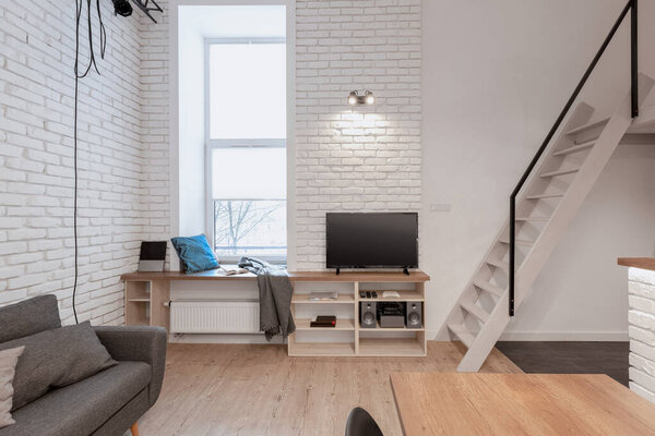 Loft style apartment with stairs to mezzanine from tv room with narrow window and white brick on the walls