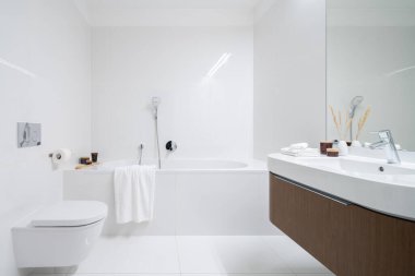 Geniş ve zarif banyo, büyük küvet, beyaz fayanslar, ahşap dolaplı lavabo ve büyük ayna.