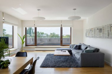 Lüks dairede geniş ve parlak bir oturma odası. Terasa açılan büyük pencere kapıları var.