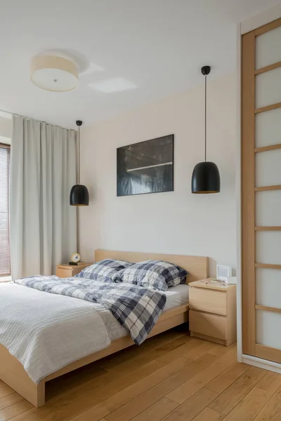 Simple bedroom with wooden floor, bed frame, bedside table and wardrobe