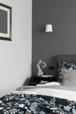 Büyük yataklı rahat yatak odası, şık komodinli kitaplar, dekorasyonlar ve gri duvarlar.