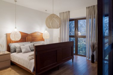 Kaliteli yataklı şık bir yatak odası, kolye lambaları ve akşamları büyük bir pencere.