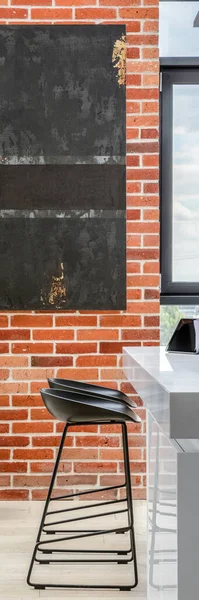 Vertical panorama of exposed red brick on kitchen wall with modern art and white kitchen table with black chairs