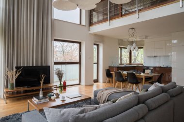 Büyük pencereli, geniş oturma odalı, televizyon ekranlı yemek masalı, mutfağa açık parlak bir daire.