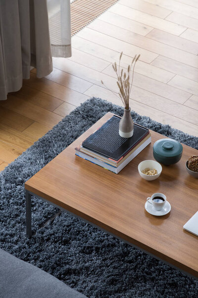 Top view on wooden and simple coffee table with books, vase, bowls and decorative containers and white cup of coffee