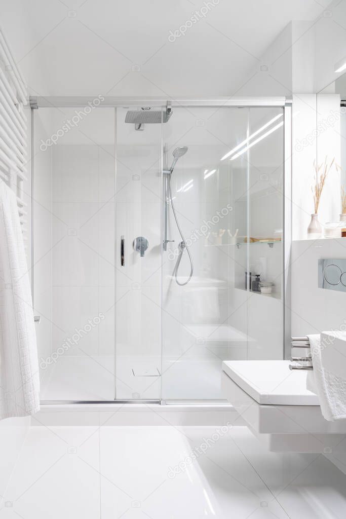 Simple bathroom in white tiles with spacious shower cabin with glass sliding doors