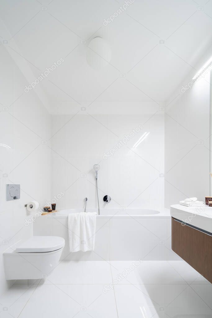 Spacious and simple bathroom in white tiles with bathtub, toilet and led lighting