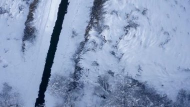 Kış boyunca karla kaplı nehir, ağaçlar ve çayırların drone görüntüsü