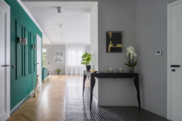 Elegant and spacious apartment corridor with nice, green walls with molding and stylish black console table with decorations