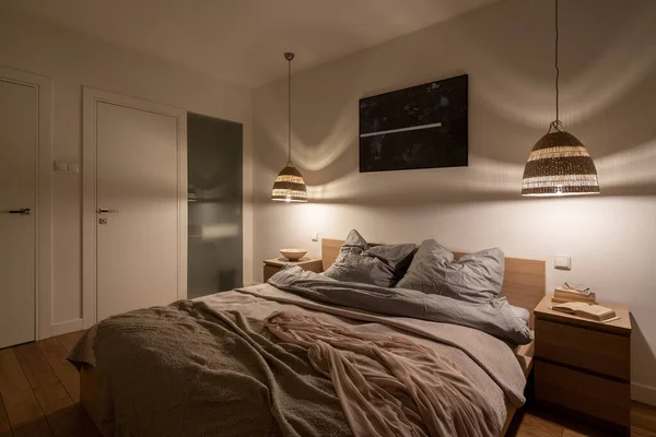 Simple and comfortable bedroom with big bed, two wooden bedside tables and two rattan lamps giving nice light