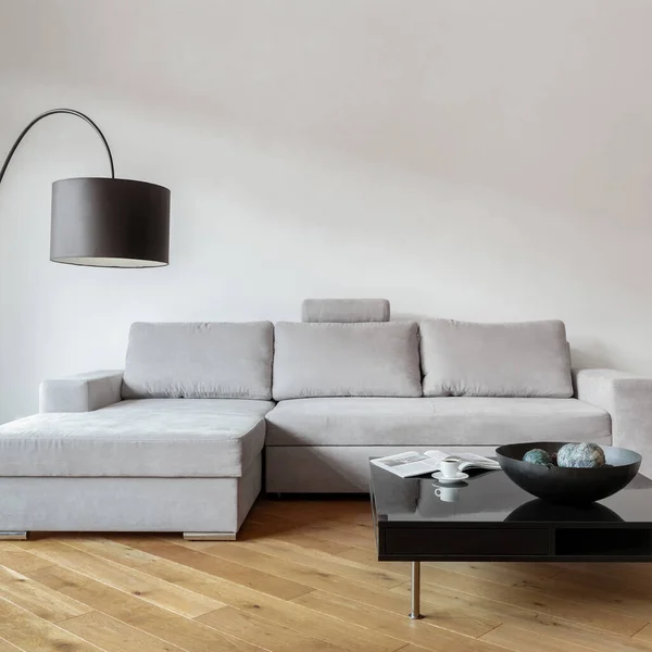 Bright living room with stylish, gray corner sofa and modern, black coffee table under black lamp