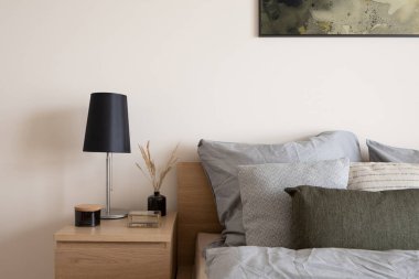 Şık, ahşap komodinli, siyah lambasıyla rahat bir yatak, dekoratif çimenli siyah vazo, süslü siyah kap ve cam mücevher kutusu.