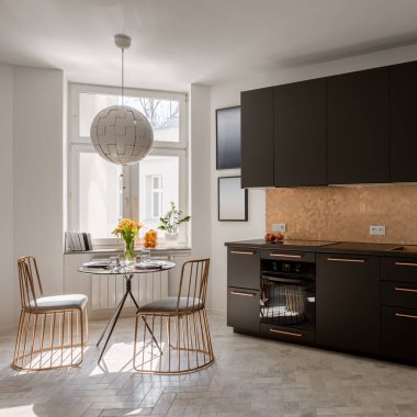 Küçük ve modern siyah mutfak, şık bakır detaylar, yeni yemek masası ve iki, zarif bakır sandalyeler ve pencere.