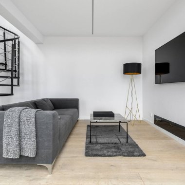 Büyük televizyon ekranlı minimalist oturma odası, basit kanepe, gri halı, cam sehpa ve şık lamba.