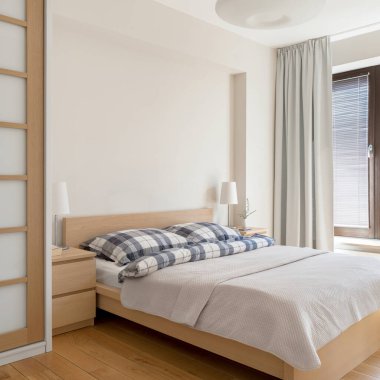 Parlak yatak odasında rahat, ahşap mobilyaları, perdeleri ve penceresi olan büyük bir yatak.