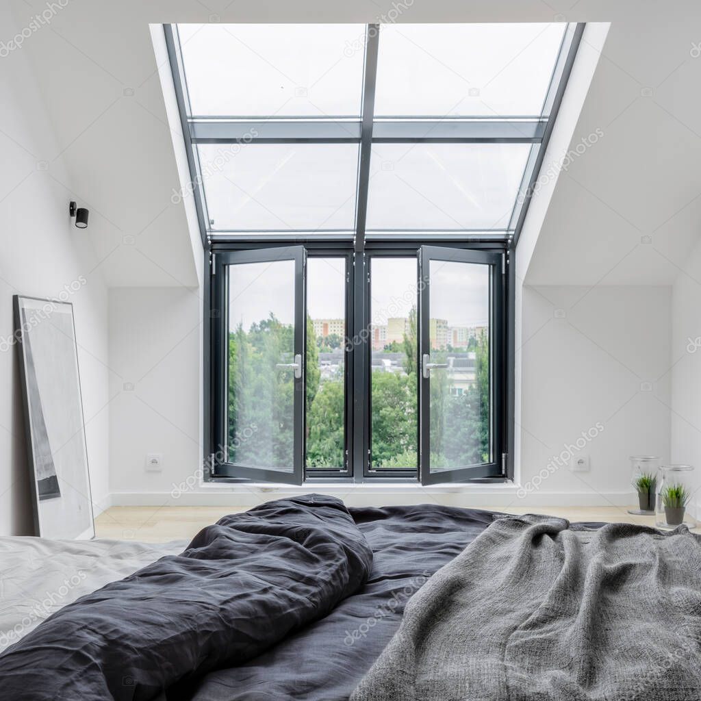 Big window in modern white attic bedroom with comfortable bed