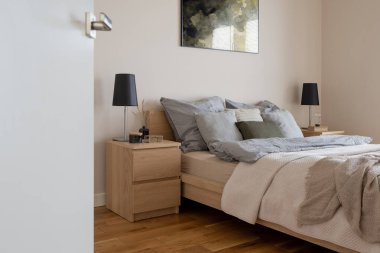 Dekorasyonlu iki ahşap komodinli rahat yatak odası ve açık kapılı, sade ve rahat bir yatak odası.