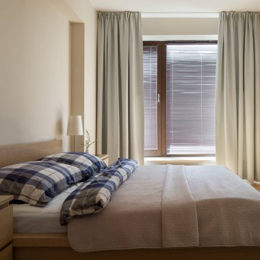 Şık, güneşli ve sade bir yatak odası rahat bir yatak odası ve ahşap panjurları ve perdeleri olan büyük bir pencere.