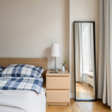 Yatağın yanında lamba ve siyah çerçeveli uzun ayna olan basit bir yatak odası.