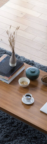 Panoramic top view on wooden and simple coffee table with books, vase, bowls and decorative containers and white cup of coffee