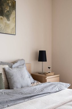 Ahşap komodindeki siyah lamba, yanında süslemeler ve gri çarşaflar.