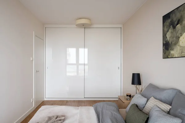 Small and simple bedroom with comfortable bed and big white wardrobe with sliding doors