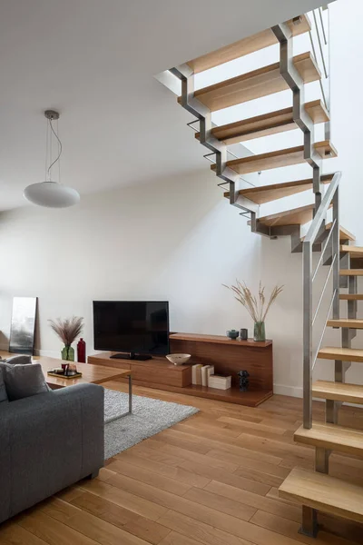 Modern living room with wooden stairs to second floor, wooden floor and furniture and big television screen
