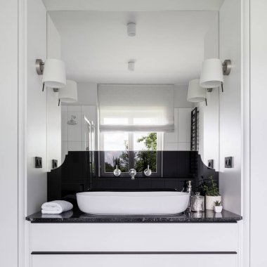 Büyük aynalı zarif siyah beyaz banyo, güzel gümüş musluklu zarif lavabo, siyah tezgah ve beyaz çekmeceler.