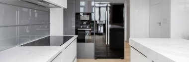 Beyaz mobilyaları, tezgahları, gri döşemeleri ve büyük siyah buzdolabı olan özel mutfak manzarası.
