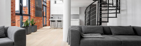 Современная лофт-квартира с обнаженной грудью на стенах, большими окнами, черной спиральной лестницей и кухней, открытой для гостиной с современным диваном и креслом