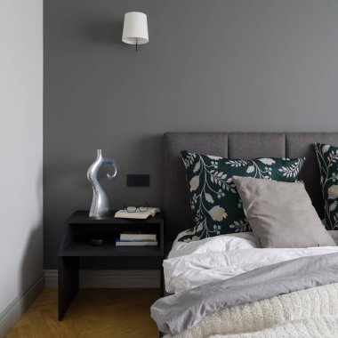 Siyah gece standına yakın plan dekorasyonlar ve zarif yatak odasında gri duvarlı ve şık ahşap zeminli.