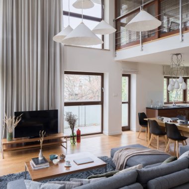 Zarif ve ferah iki katlı büyük pencereli, uzun perdeli, şık kolye lambalı, oturma odasında televizyon ve yemek salonu olan bir daire.