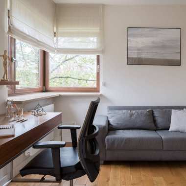 Pencereli şık ofis odası, rahat gri kanepe ve siyah sandalyeli ahşap masa.