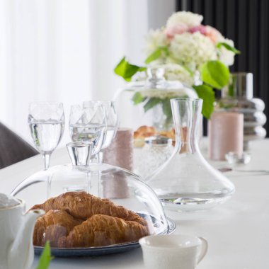 Cam, tencere, sürahi, bardak, çiçek ve yiyecekle süslü yemek masasına yakın plan.