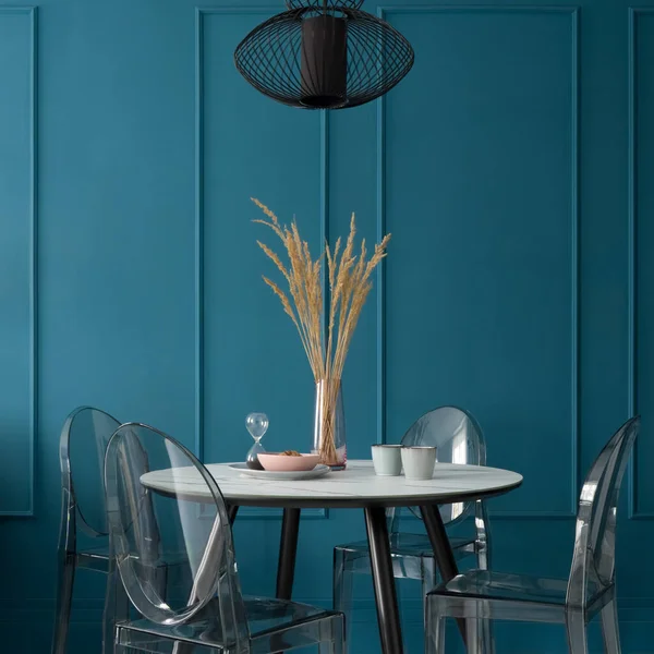 Fancy dining room with blue wall with molding and with modern table with black legs and marble style countertop, nice table decorations, four, new plastic chairs under black pendant lamp