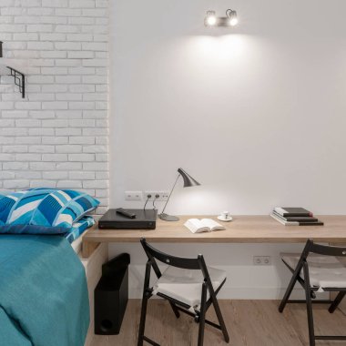 Yatak odasında mavi çarşaflı, duvarında beyaz tuğla olan iki kişilik basit ahşap masa.