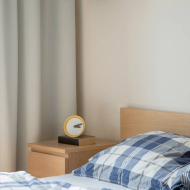 Parlak yatak odasındaki ahşap komodinin sarı saatine yakın plan.