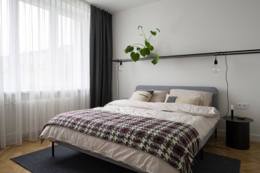 Basit dekore edilmiş yatak odası, büyük rahat yatak odası, modern komodin ve beyaz perdelerin arkasındaki büyük pencere.