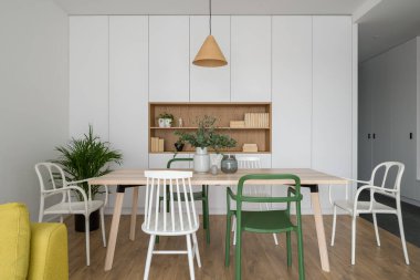 Basit ve güzel yemek odası, uzun ahşap masa, farklı ve şık, beyaz ve yeşil sandalyeler.