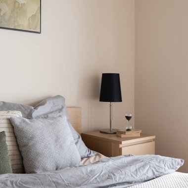 Sade, ahşap komodinin üzerinde, rahat yatağın yanında gri çarşaflarla süslenmiş siyah lambaya yakın plan.