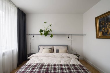 Parlak ve basit tasarlanmış yatak odası. Sanat, pencere ve siyah rafın altında ampulleri olan rahat yatak odası.