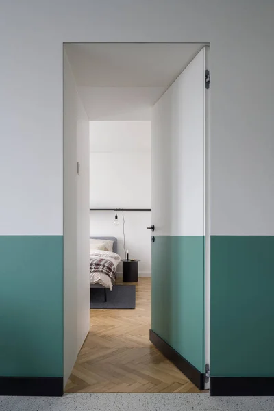 Stylish white and green doors open to spacious and bright bedroom with wooden floor and comfortable bed