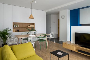 Basit ve modern yemek masası renkli ve farklı sandalyeler şık oturma odasında televizyonu mutfak alanına açık.