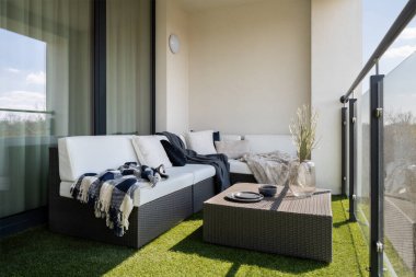 Güzel balkon. Köşesinde kanepe, sehpa ve yerde sentetik çimenler var.