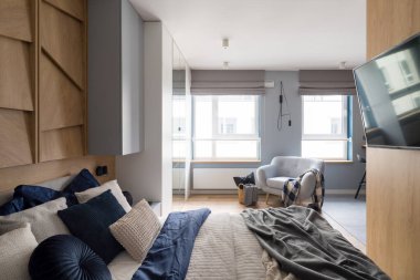 Şık yatak odası, rahat yatak odası, güzel çarşaflar, büyük pencereler, rahat koltuklar ve ahşap duvarda televizyon.