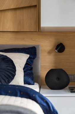 Güzel vazo, yatak odasında ahşap duvarlı şık çarşaflı rahat yatağın yanındaki basit komodinin üstünde.