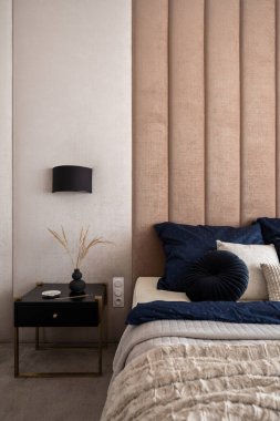 Güzel yatak odası, şık, siyah komodinli siyah masa, siyah lambanın altında süslü yatak örtüleri ve döşemeleri olan rahat yatağın yanında.