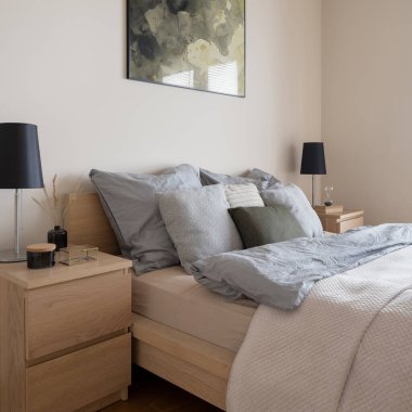 Rahat bir yatağa yakın çekim, iki ahşap komodin, parlak yatak odasında siyah lambalar ve dekorasyonlar.